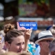 Iowan holds "Make Him Go Away for 2020" sign at state fair during Democratic presidential candidates visit.