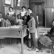 African American children learning about Thanksgiving, with model log cabin on table, Whittier Primary School, Hampton, Virginia. Photograph by Frances Benjamin Johnston, [1899 or 1900].