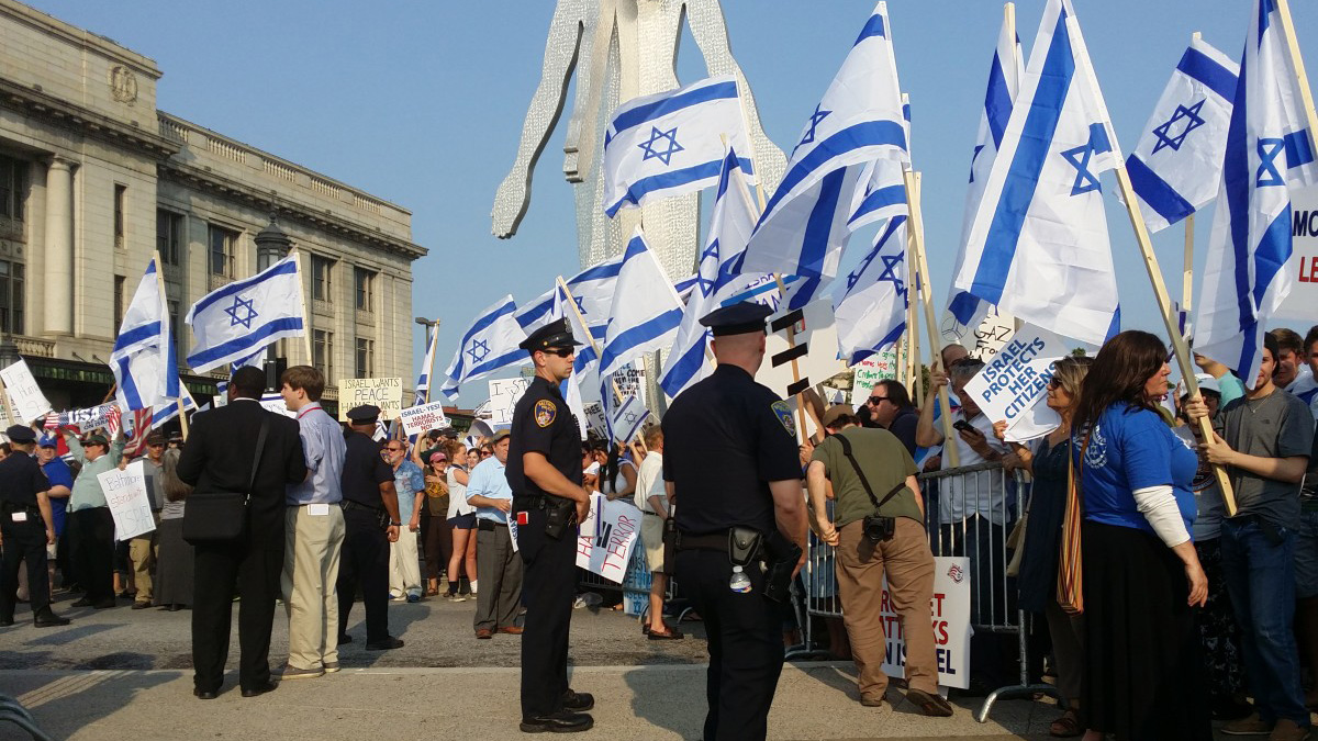 Protestors wave signs and the flag of Israel.