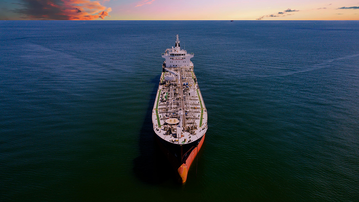 Aerial photo of large oil tanker at sea, with a colorful sunset shown on the horizon.